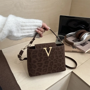 Brown leopard print crossbody tote bag with gold V-buckle on a minimalist desk