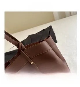 Close-up of brown tote bag showing fine stitching and gold metal pendant detail