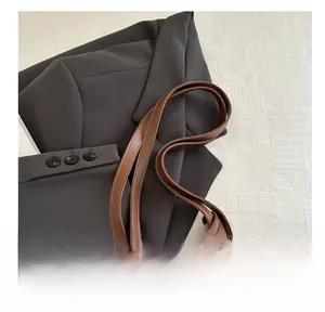 Detail of brown leather tote bag showing sturdy double handles and gold metal ring hardware