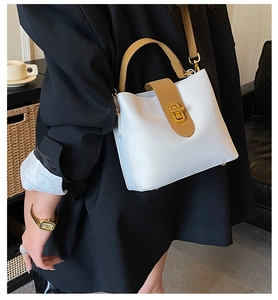 Detail of white and brown bucket bag with gold twist lock held by a model in a suit