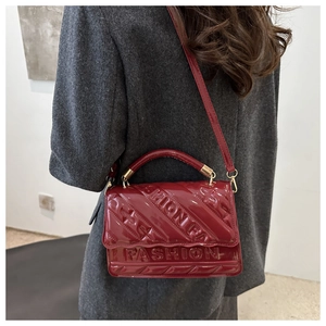 Detail van de wijnrode lakleren handtas met 3D-stikselpatroon en reliëfletters op de tas