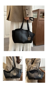 Detail of black tote bag with gold M pendant on long handles for casual commute