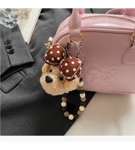 Detail of plush bear charm with polka dot bow attached to pink leather shoulder bag