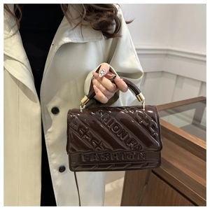 Detail van het FASHION-logo in reliëf op de donkerbruine lakleren handtas met glans