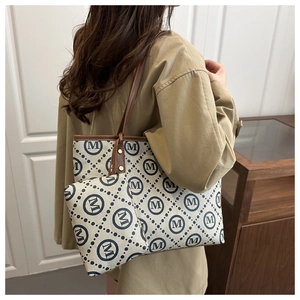 Model wearing a large canvas tote bag and matching pouch with blue monogram pattern