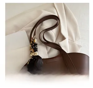 Detail of a brown tote bag featuring a decorative printed silk scarf on the handle