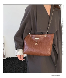 Detail of brown woven tote bag featuring a gold deer pendant and metallic chain strap