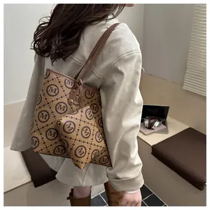 Detail shot of caramel brown tote and matching pouch with M logo print on woman's shoulder