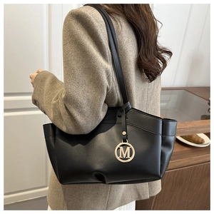 Close-up of black leather tote bag featuring gold M-letter charm and slim shoulder straps
