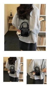 Detail of black glossy mini bag with dog embossing, plush charm and pearl chain