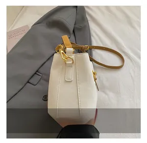 Detail of cream bucket bag featuring polished gold hardware and brown leather straps