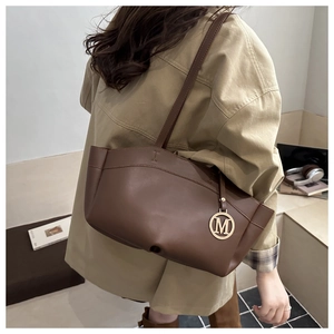 Close-up of dark brown leather tote bag featuring a golden metallic M charm detail