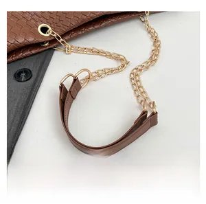 Detail of brown woven shoulder bag strap with gold chain links and leather stitching
