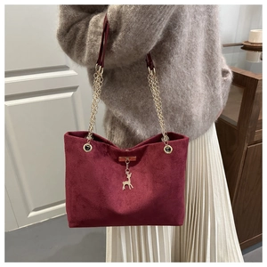 Detail of wine red suede shoulder bag with golden deer charm and chain strap on model
