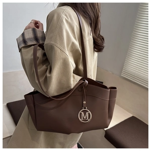 Brown leather tote bag styled with a beige trench coat featuring a metal M charm