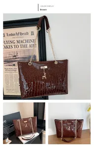 Detail of coffee crocodile embossed tote bag featuring a gold chain strap and deer charm