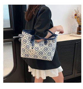 Détail du sac cabas en toile avec imprimés M et bandoulière porté par un mannequin