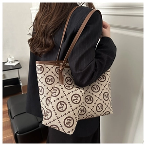 Detail of large canvas tote bag with M-letter print and brown leather shoulder straps