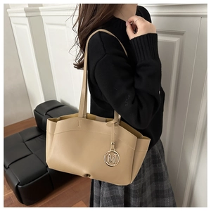 Detail of beige faux leather tote bag with metallic M charm and textured finish