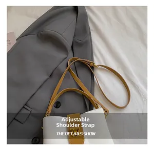 Detail of adjustable brown leather shoulder strap and gold metal buckle on white bucket bag