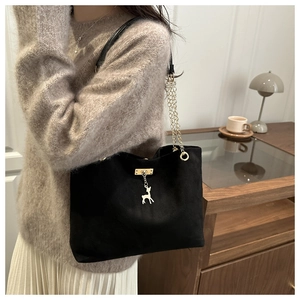 Close-up of matte black suede shoulder bag featuring a golden deer charm and chain strap