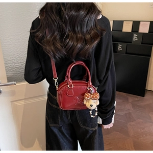 Close-up of wine red glossy leather handbag with a teddy bear charm and strap