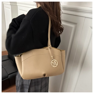 Detail of beige faux leather tote bag with golden letter M charm on the shoulder strap