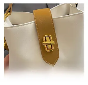 Detail of golden turn-lock closure on white pebble leather bucket bag with brown trim