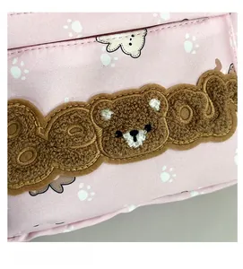 Detail of pink backpack featuring bear plush embroidery and white paw prints patterns