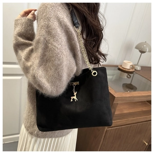 Detail of black suede tote bag with golden deer charm and chain strap in casual setting