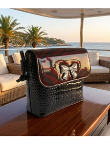 Detail of crossbody bag with crocodile texture and silver bow buckle on wooden table