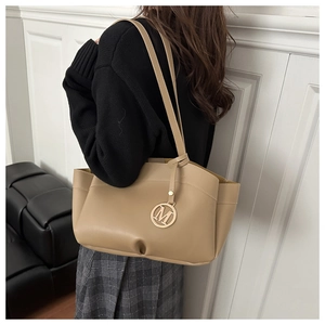 Detail of khaki leather tote bag featuring a round metallic letter M charm and shoulder strap