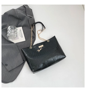 Detail of black croc-embossed tote bag with gold chain strap and deer charm accessory