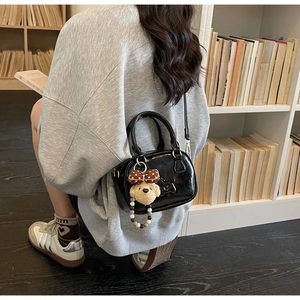 Detail of glossy black bowling bag with a cute teddy bear charm on a grey outfit