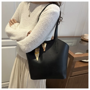 Detail of a black leather bucket bag with a silk scarf tied on the handle for luxury styling
