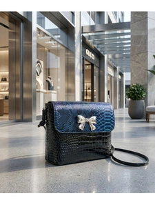 Detail of snake skin pattern flap and golden bow buckle on black crossbody bag