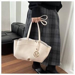 Detail of beige leather tote bag with wavy edges and gold metallic M-shaped charm