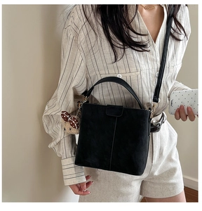 Detail of black matte bucket bag featuring a plush bear pendant and vertical stitching