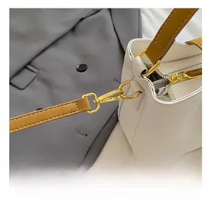 Detail shot of the gold metal hook and brown strap on a white leather bucket handbag
