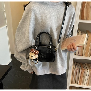 Detailed view of black patent leather mini bowling bag with cute plush bear charm