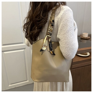 Detail of a large khaki leather tote bag featuring a silk scarf on the shoulder strap