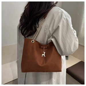 Détail du sac cabas en velours côtelé marron avec chaîne dorée et breloque cerf sur l'épaule