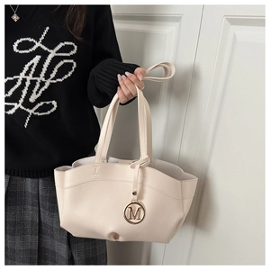 Detail of cream tote bag featuring a gold M-pendant and smooth leather texture