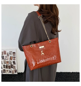 Detail of red-brown crocodile pattern bag featuring gold chain and deer pendant