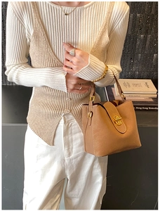 Detail of camel leather bucket bag featuring a gold twist lock and D-ring shoulder strap