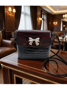 Detail of crossbody bag with crocodile texture and zebra print flap with silver bow