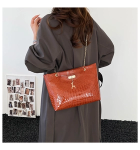 Detail of crocodile pattern brown tote bag with a gold deer pendant and stylish chain strap