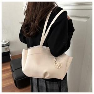Detail of a creamy white leather tote bag with a golden M charm shown on a model