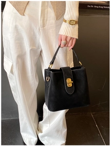 Detail of a black bucket bag with a golden turn-lock closure held by a model