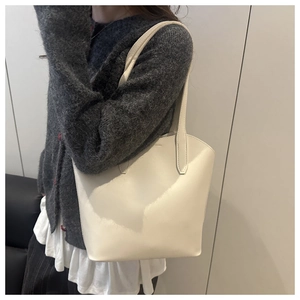 Close-up of minimalist beige tote bag with slim shoulder strap worn by a model